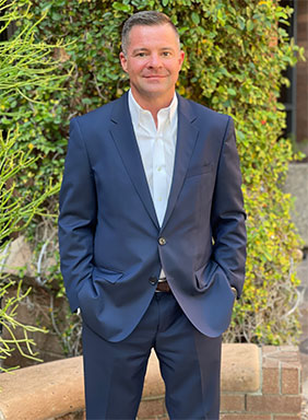 professional headshot of Dr. Ranson wearing a suit in front of a green shrub